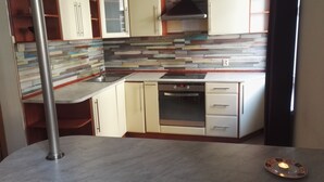 A compact kitchen with a built-in oven, a stovetop, and a microwave. There is a wooden cabinet with a glass door and a stainless steel sink. The backsplash is made of variously colored tiles. - Apartamenty Gdańsk - Apartament Ogarna (Gdansk)
