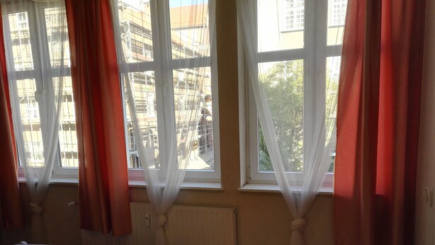 A bedroom with a bed, two windows with curtains, a radiator, and a view of buildings outside. - Apartamenty Gdańsk - Apartament Ogarna (Gdansk)