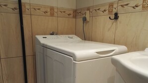 A compact, white washing machine in a bathroom with tiled walls and a toilet. - Apartamenty Gdańsk - Apartament Ogarna (Gdansk)