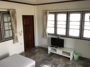 A room with a bed, a TV on a white stand, a door, and windows with curtains.