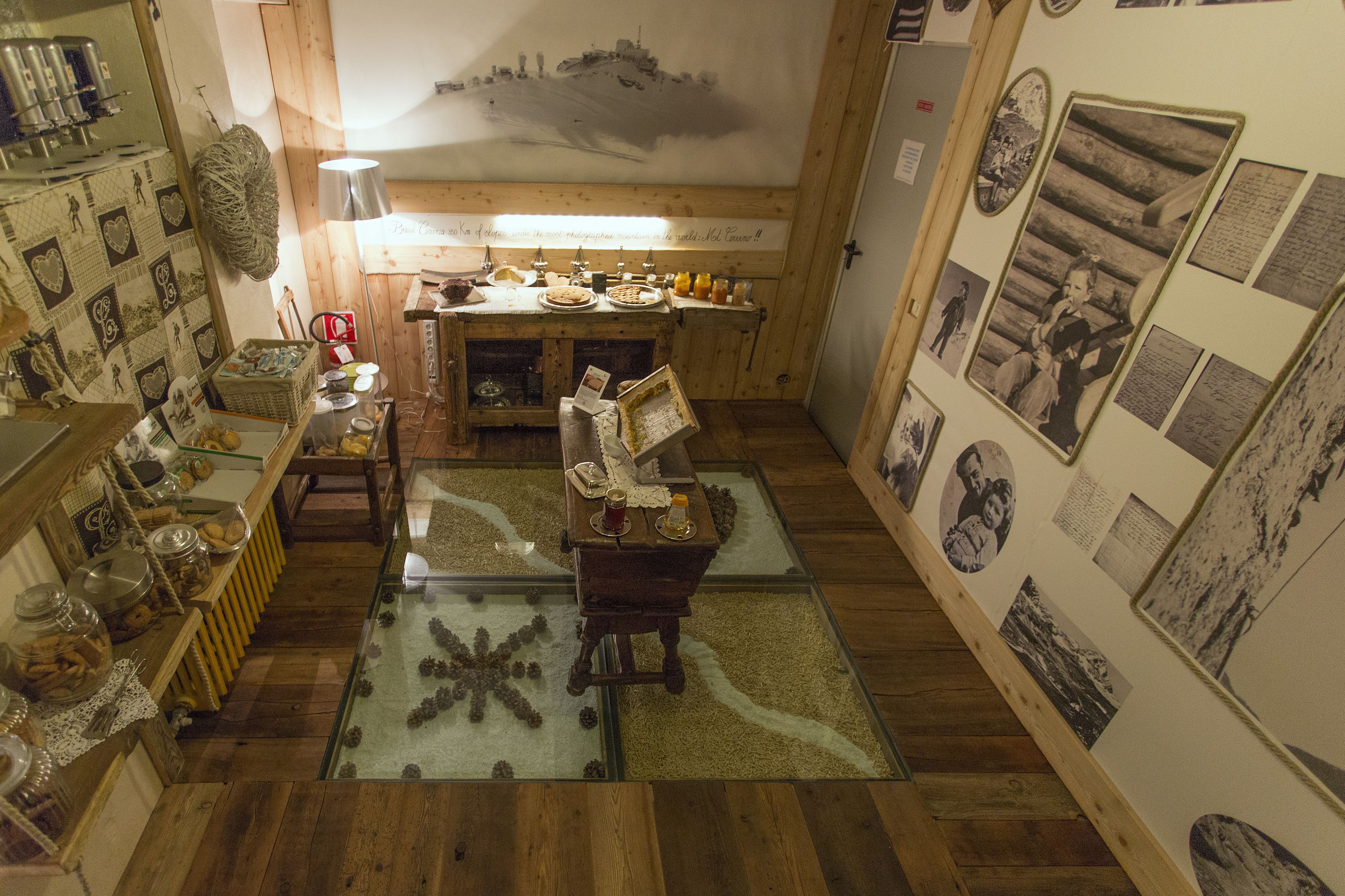 A cozy room with wooden flooring, a glass-top table with a starfish decoration, a wooden bench, and a wall adorned with framed photos and documents.
