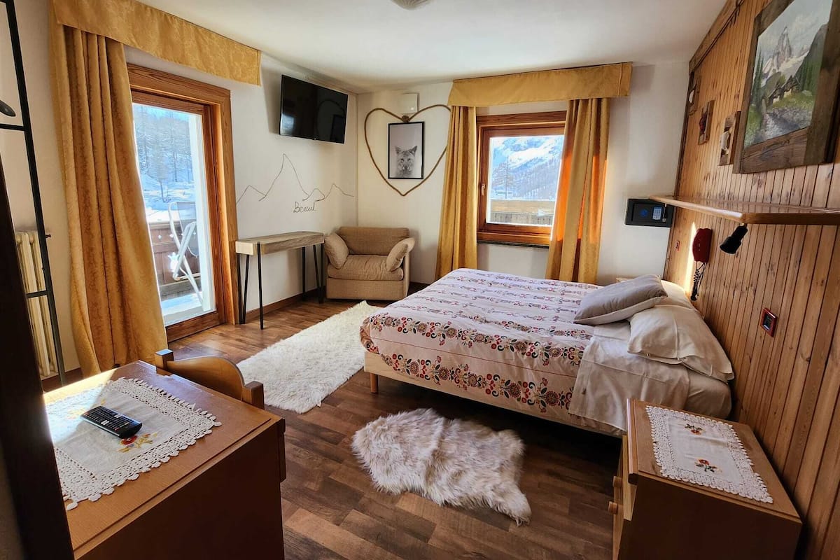 A cozy bedroom with a bed, a chair, a desk, and a TV.