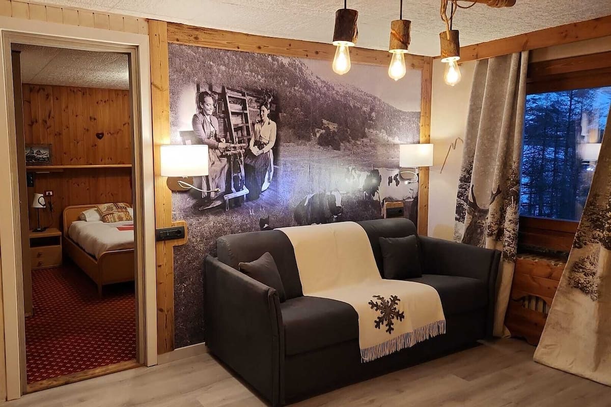 A cozy room with a bed, a sofa, and a wall-mounted lamp.