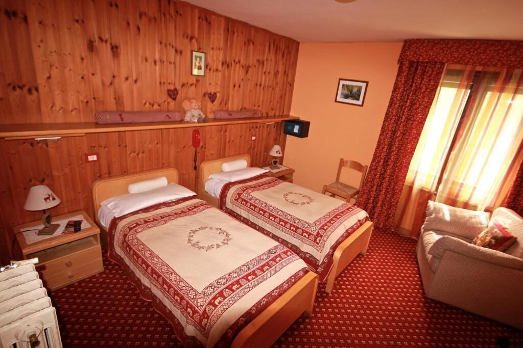 A room with two beds, wooden paneling on the walls, a small desk with a lamp, and a chair.