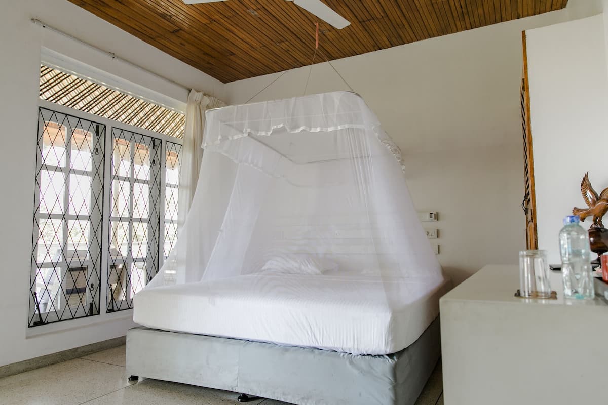 A bedroom with a bed covered by a white canopy, a wooden ceiling, and a window with a metal grid.