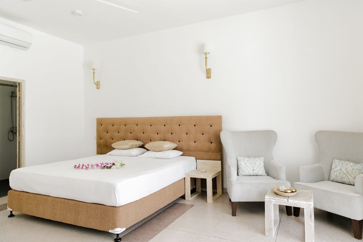 A bedroom with a large bed, two armchairs, a small table, and a nightstand.