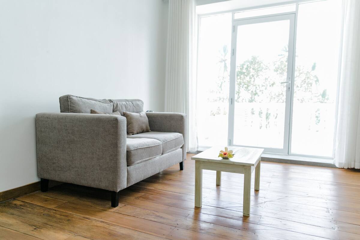 A living room with a grey sofa, a wooden coffee table, and a large window with a view of trees.