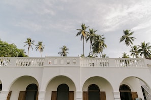 Edifício branco com janelas e varandas em arco, cercado por palmeiras.