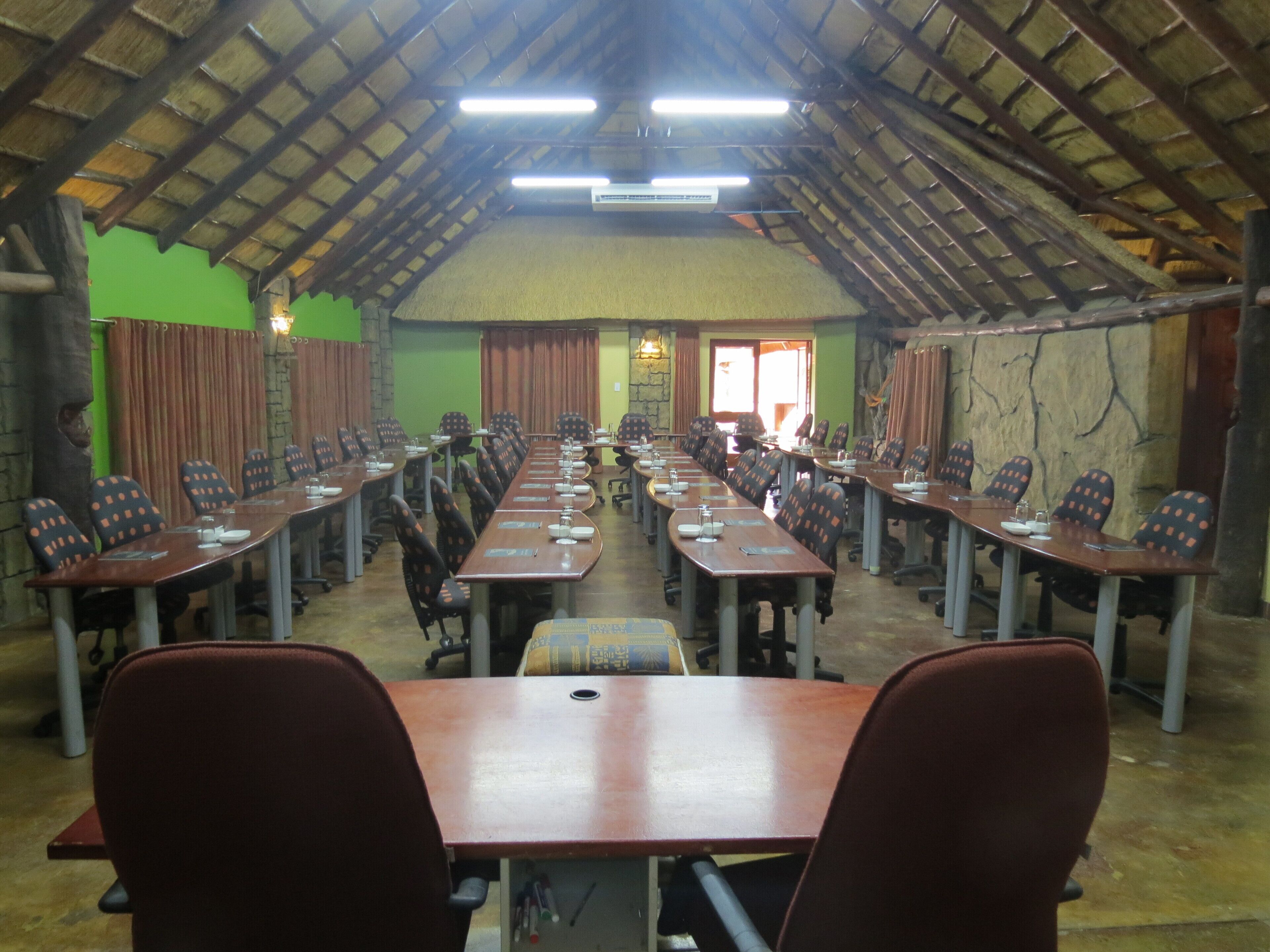 A conference room with long tables and chairs, a high ceiling with wooden beams, and green walls.