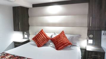 Une chambre à coucher avec un grand lit, deux oreillers rouges, une tête de lit blanche et une table de chevet avec une lampe.
