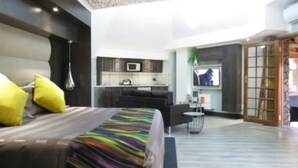 A modern hotel room with a large bed, a small kitchen area, and a seating area with a television. - Bushmans Rock Country Lodge (Roodeplaat)