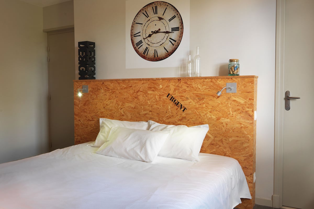 Un dormitorio con cabecera de madera que dice "URGENT", un reloj de pared grande y una puerta a la derecha.