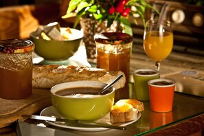 A breakfast setting with a bowl of soup, a glass of orange juice, a glass of tea, and a pastry on a wooden table.