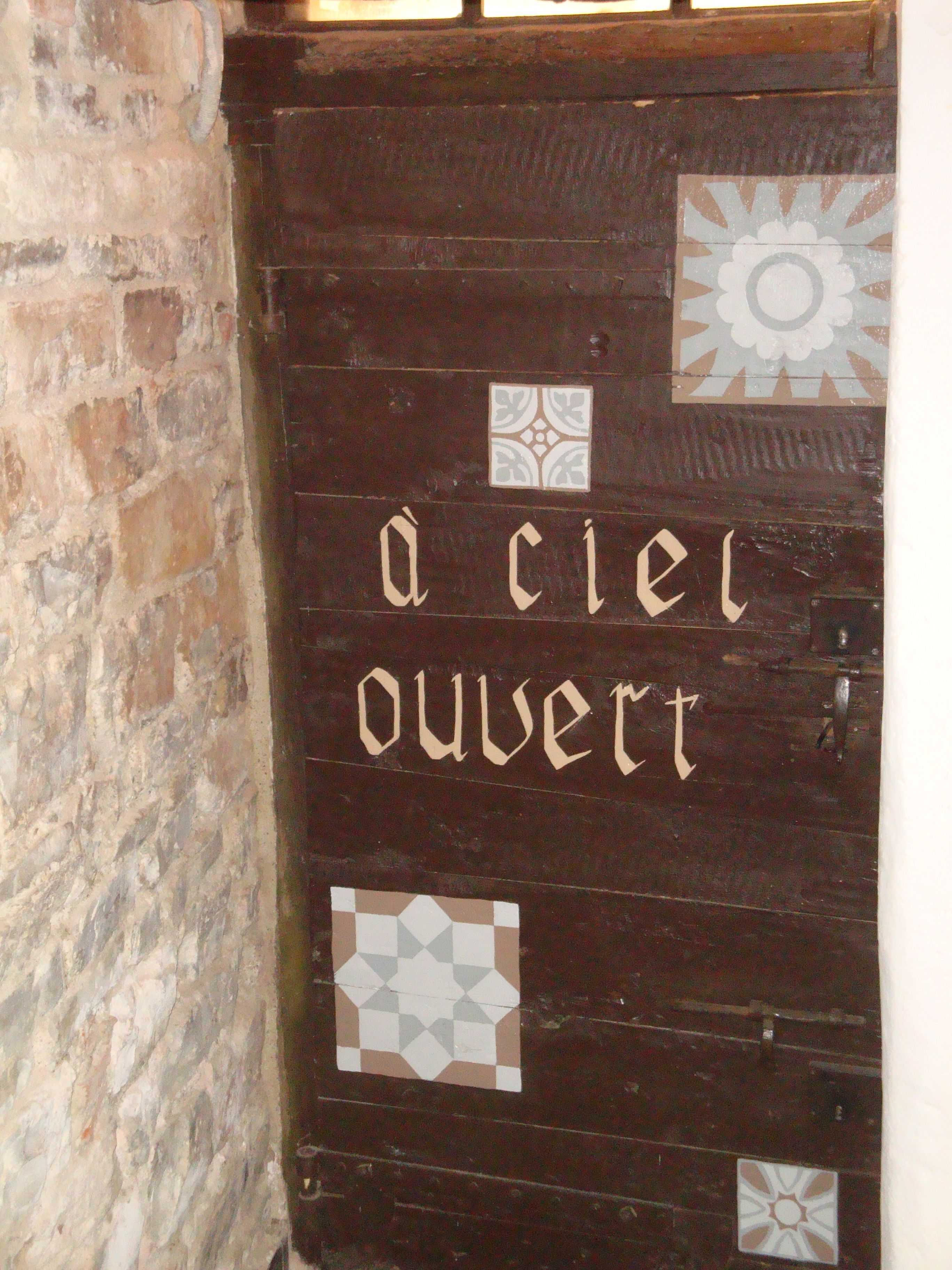 Eine Holztür mit der Aufschrift „à ciel ouvert“ und dekorativen Fliesen.