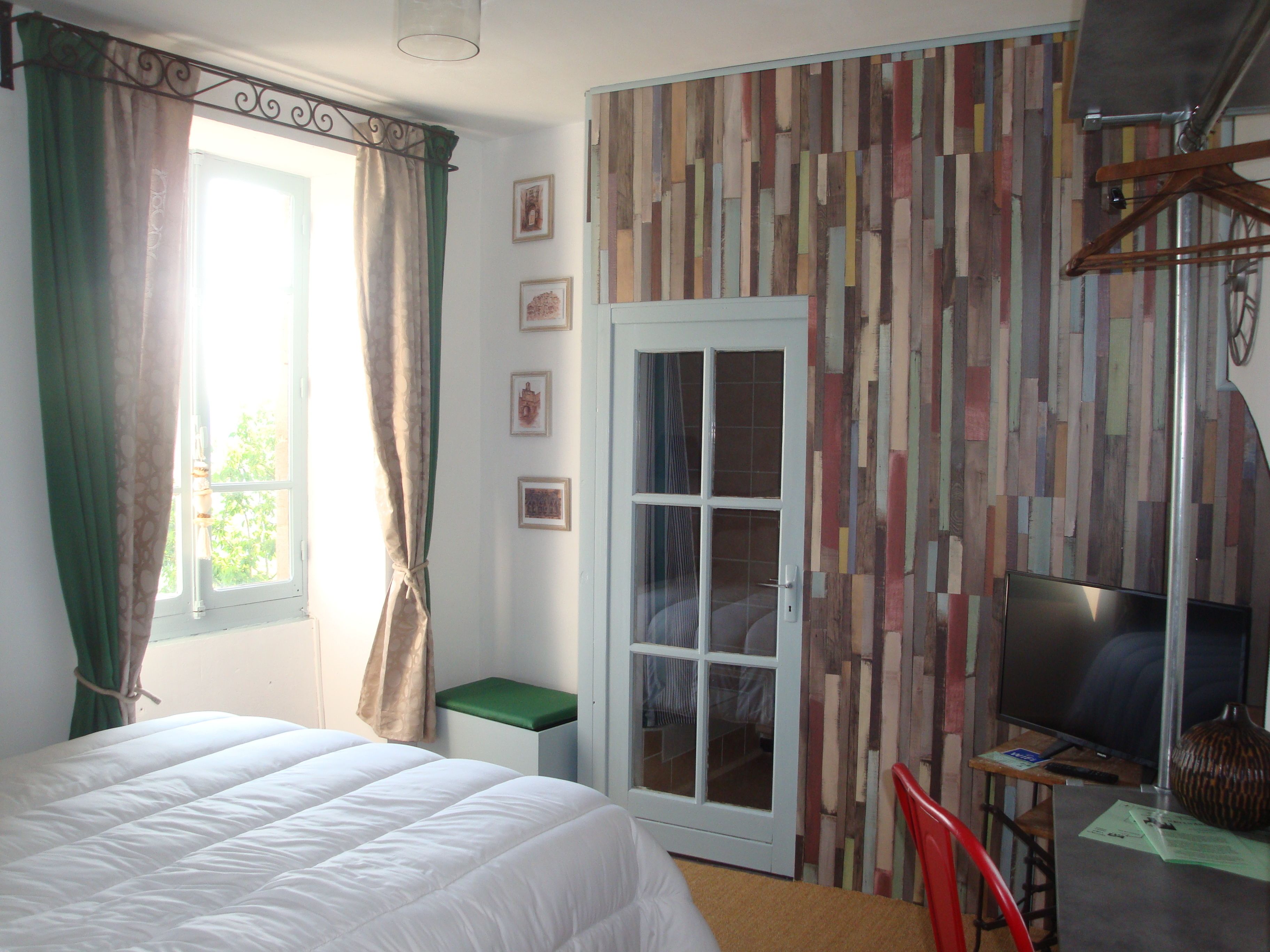 A bedroom with a bed, a desk with a chair, a television, and a door leading to another room.