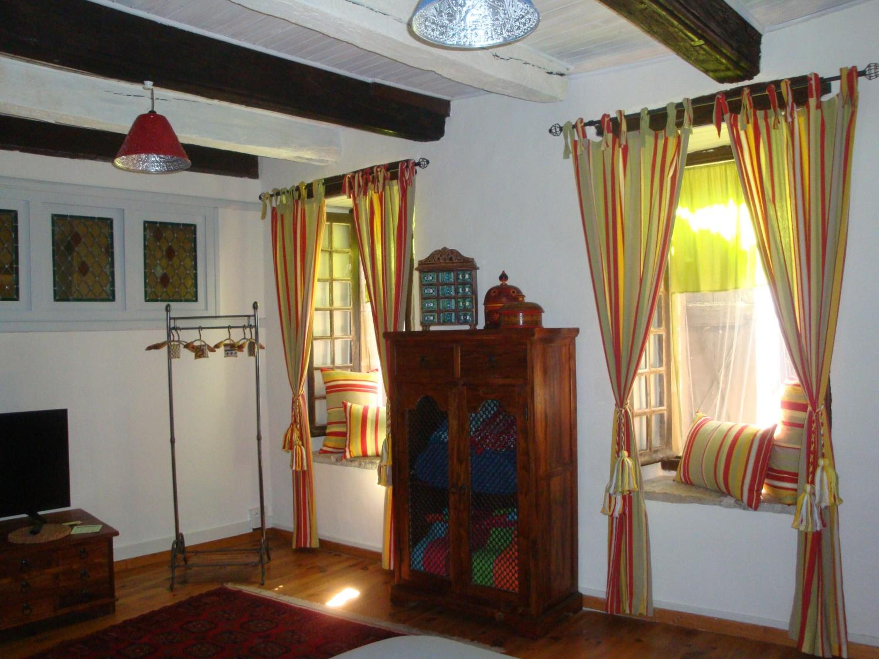 Ein Zimmer mit Holzschrank, roter Pendelleuchte, Fenster mit gestreifter Gardine und Holzboden.