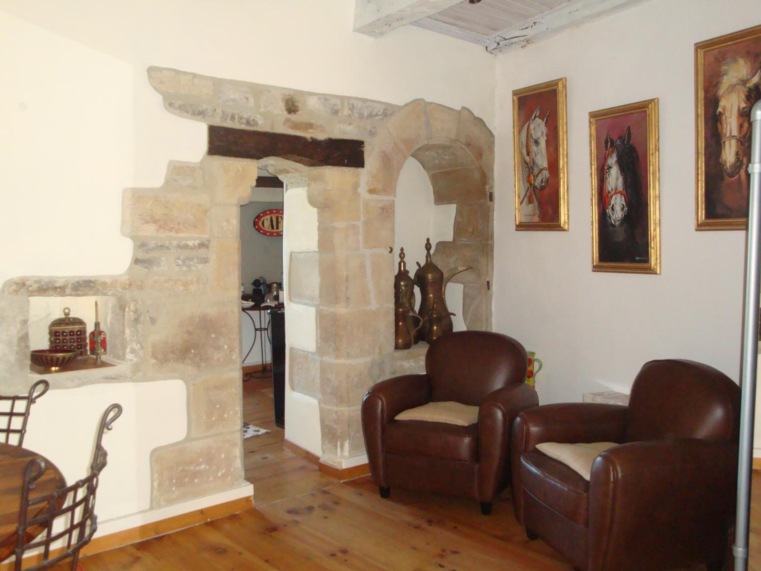 A living room with a stone archway, leather armchairs, a coffee table, and a dining area with a metal chair and table.