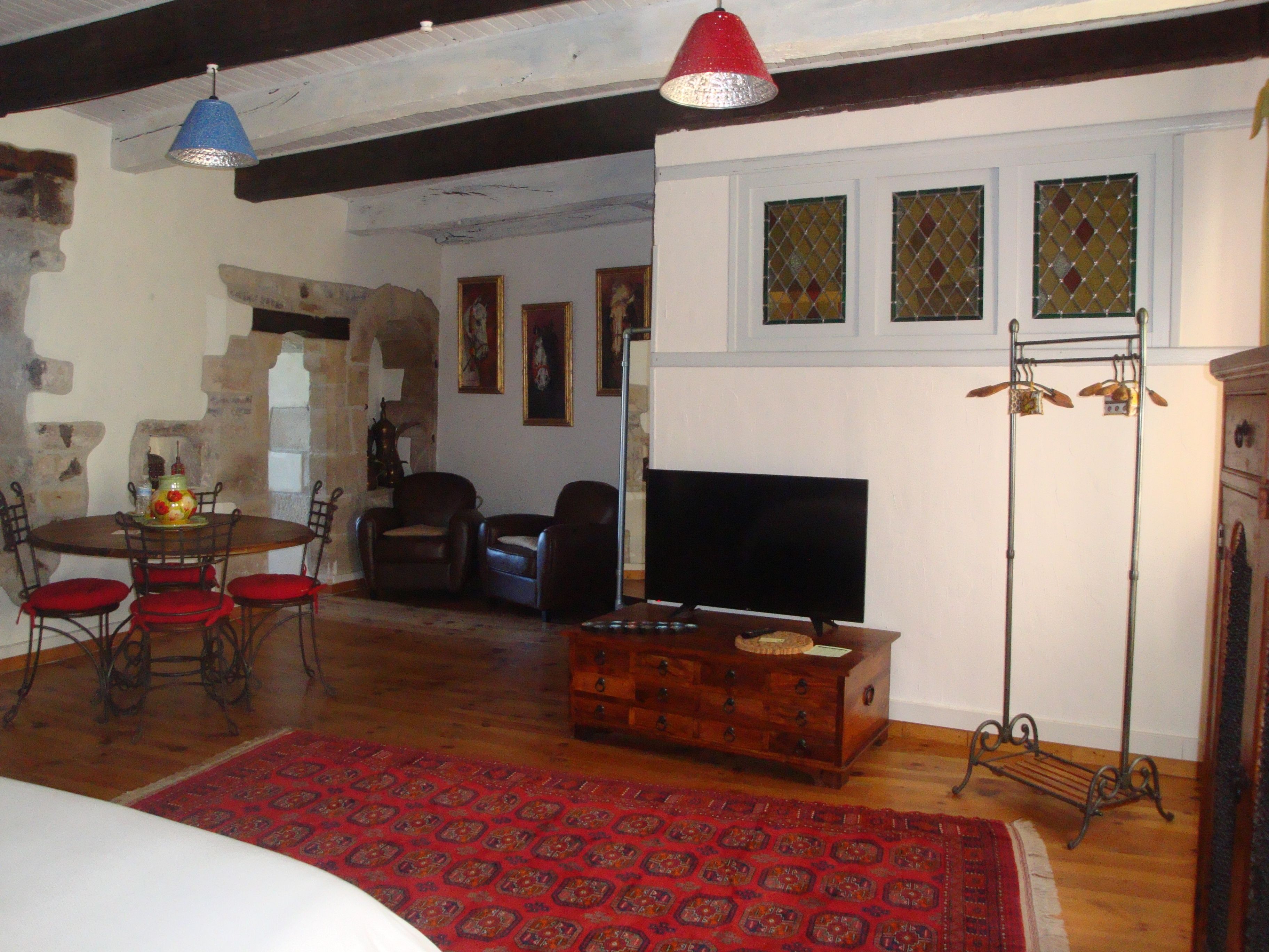 A cozy living room with a wooden dining table, red chairs, a TV, and a red patterned rug.