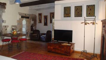 A cozy living room with a wooden dining table, red chairs, a TV, and a red patterned rug.