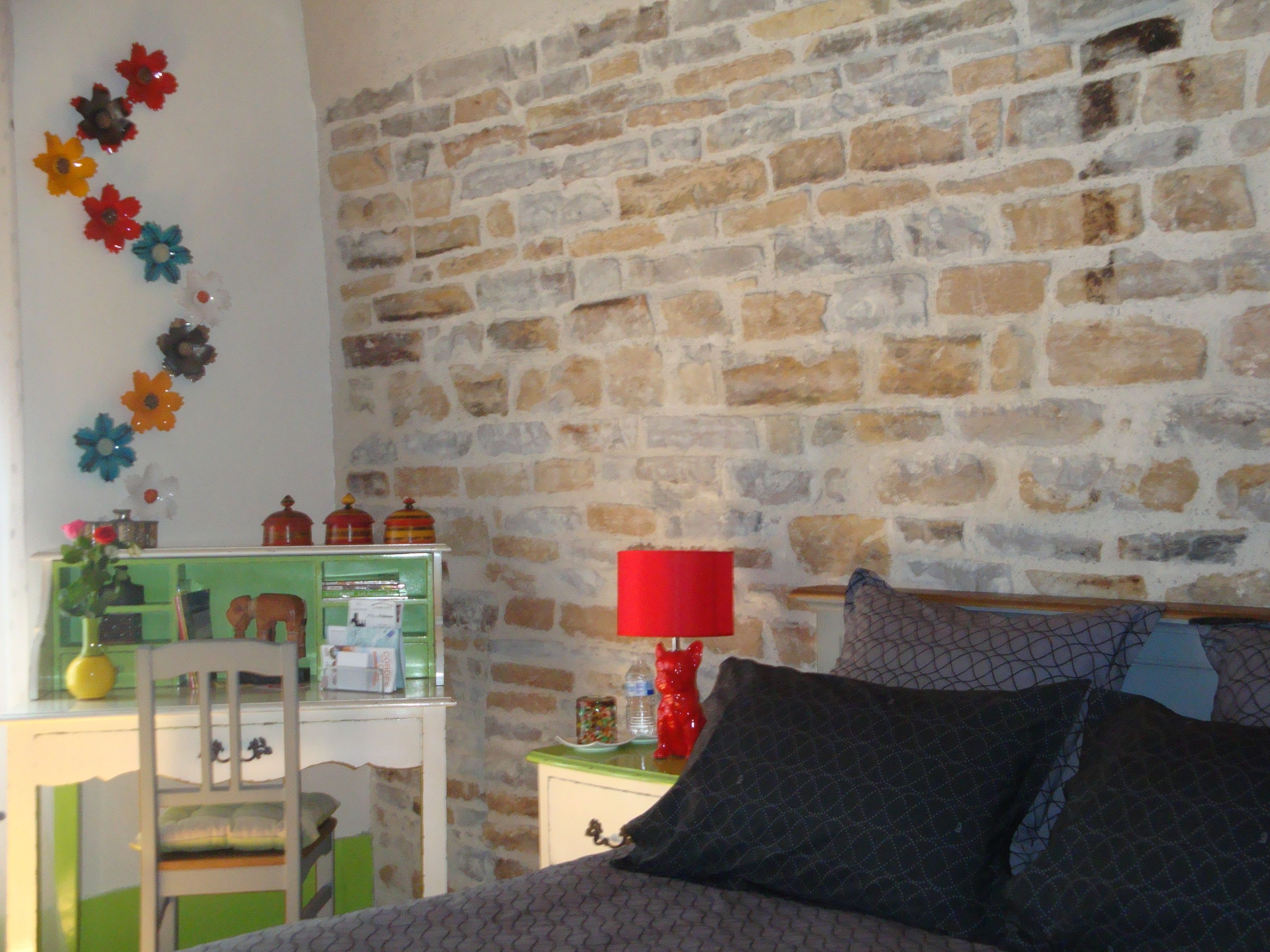 Une chambre avec un mur en briques, un bureau avec une chaise, un lit avec des oreillers et une décoration florale fixée au mur.