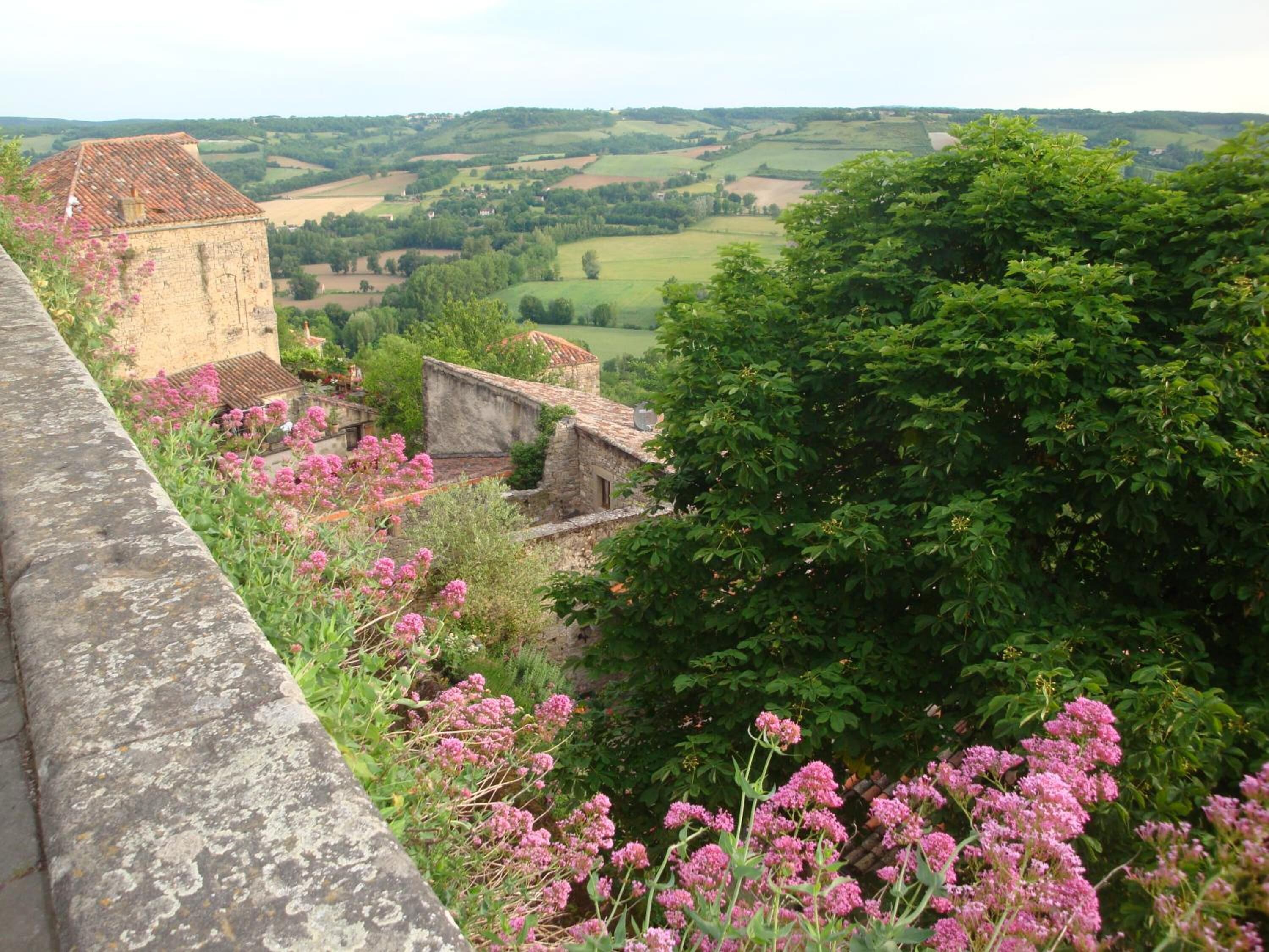 Eine Steinsichtmauer mit Blick auf eine ländliche Landschaft, darunter Felder und ein kleines Gebäude mit einem Ziegeldach.