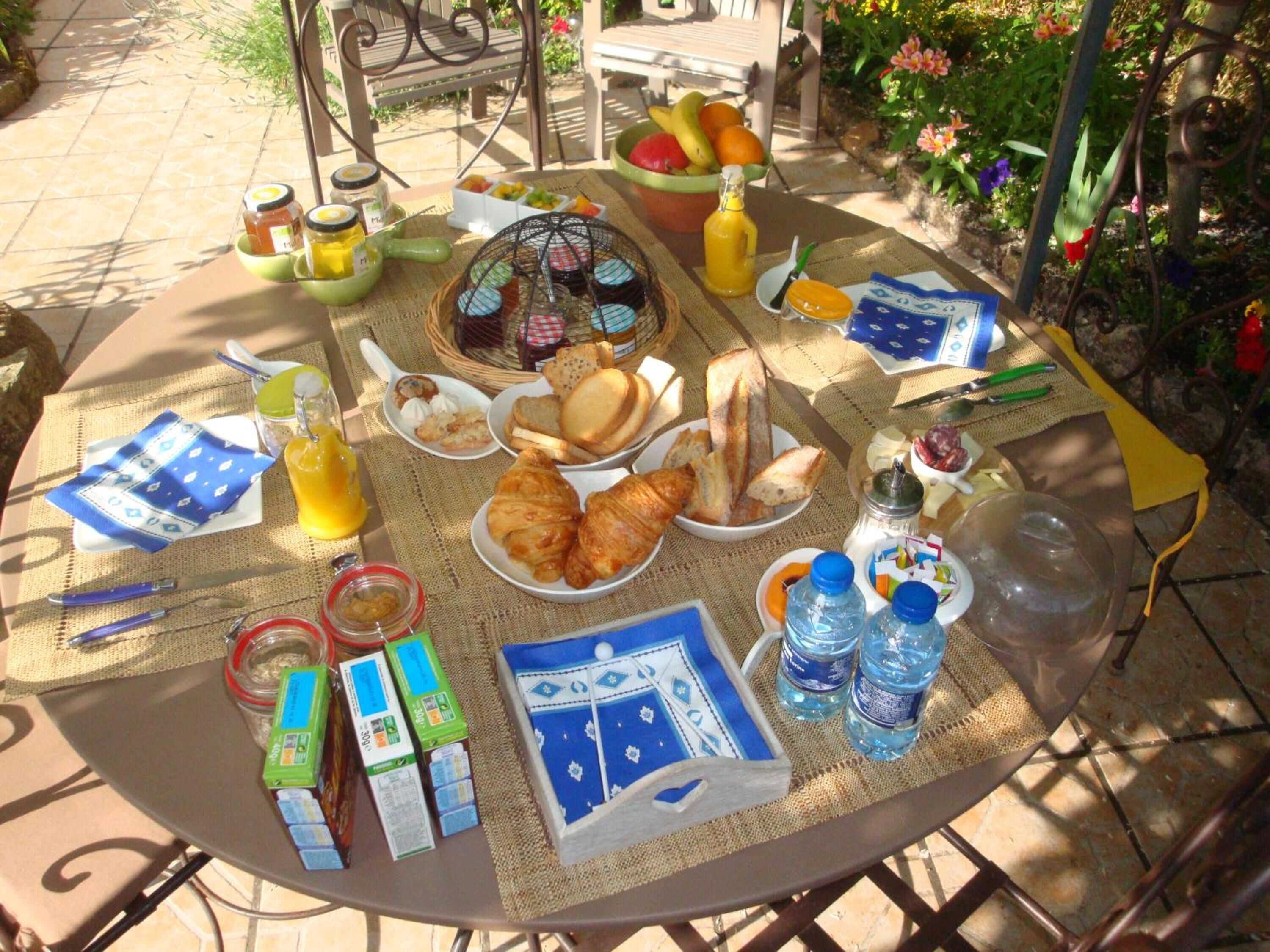 A round table set outdoors with breakfast items like bread, pastries, and fruit.