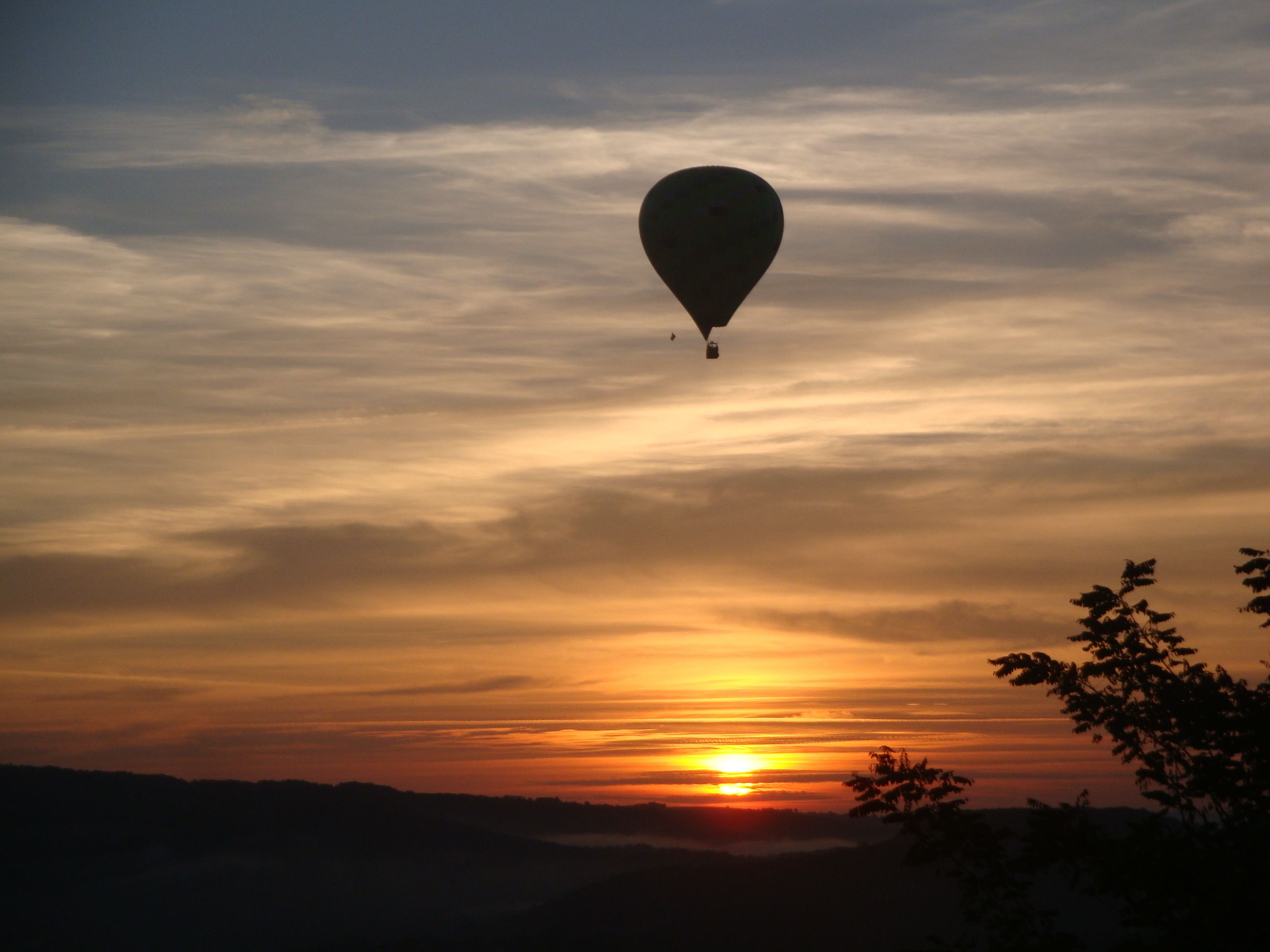 Een luchtballon boven een zonsondergang, met een silhouet van heuvels op de achtergrond.