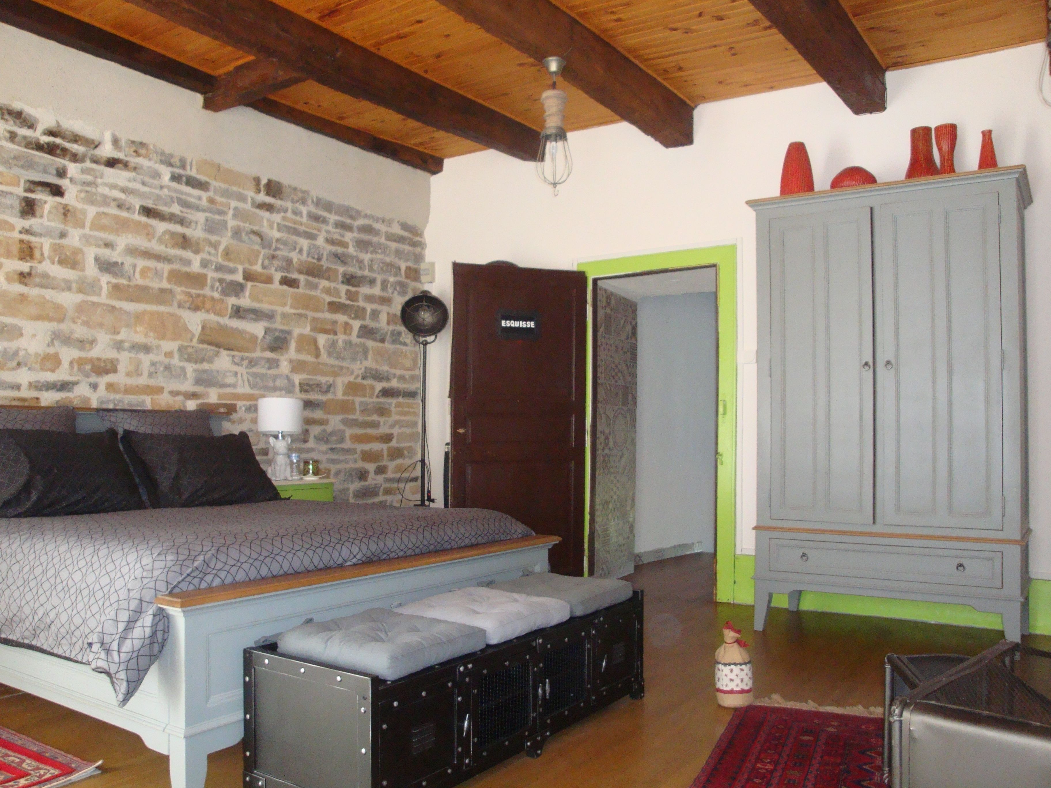 Un dormitorio con pared de piedra, cama con colcha estampada, techo de madera, un armario y un pequeño objeto decorativo.