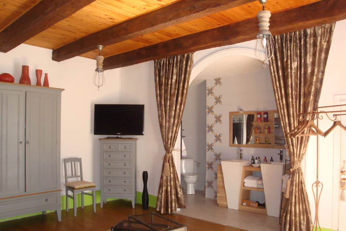 Ein Wohnzimmer mit Fernseher, Schrank, Sessel, Tisch und einem durch einen Bogen sichtbaren Badezimmer.