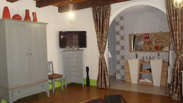Een kamer met houten plafond, een televisie op een kast, een bureau en een badkamer met spiegel en planken.