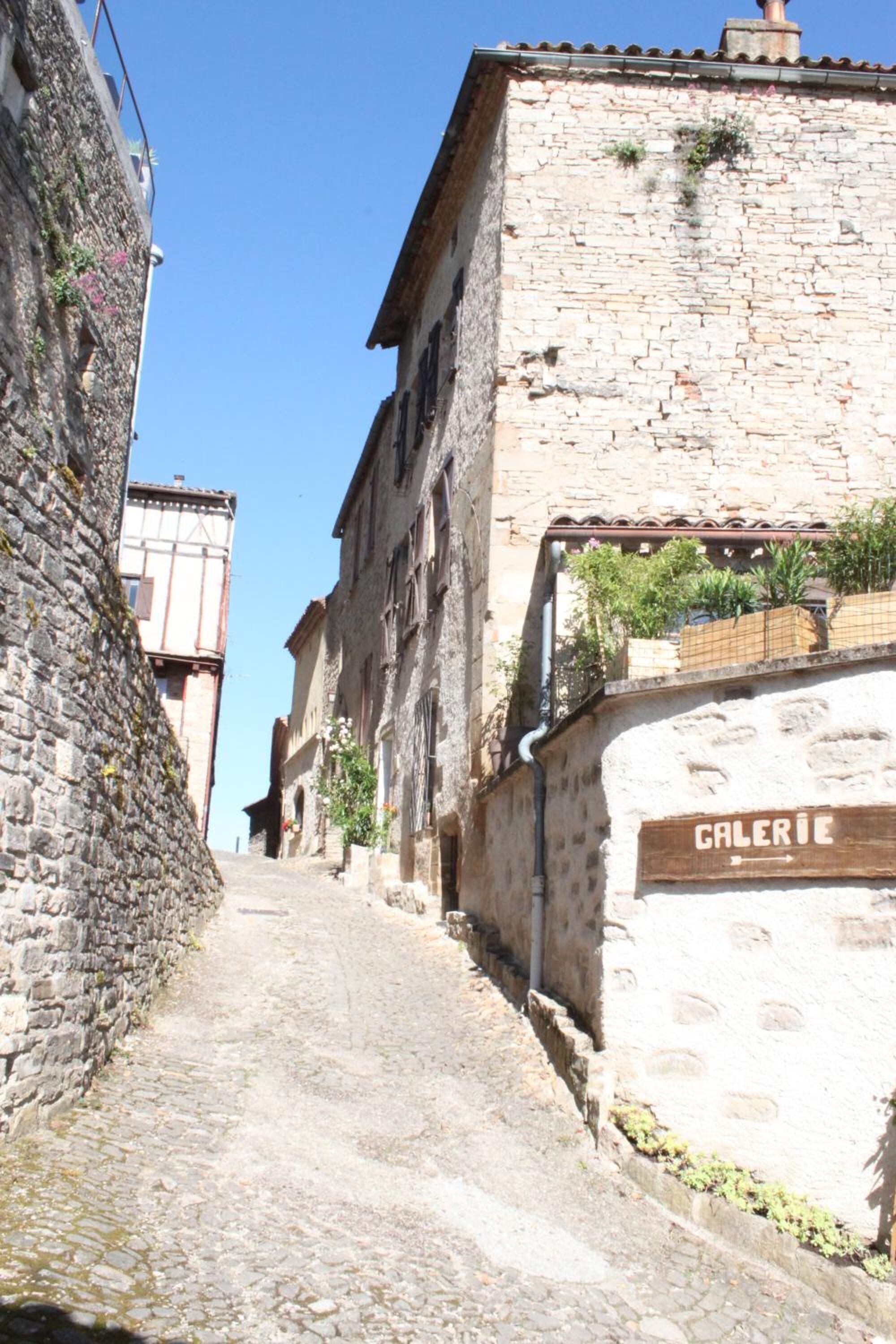 A narrow cobblestone street flanked by historic stone buildings with a sign reading "GALERIE".