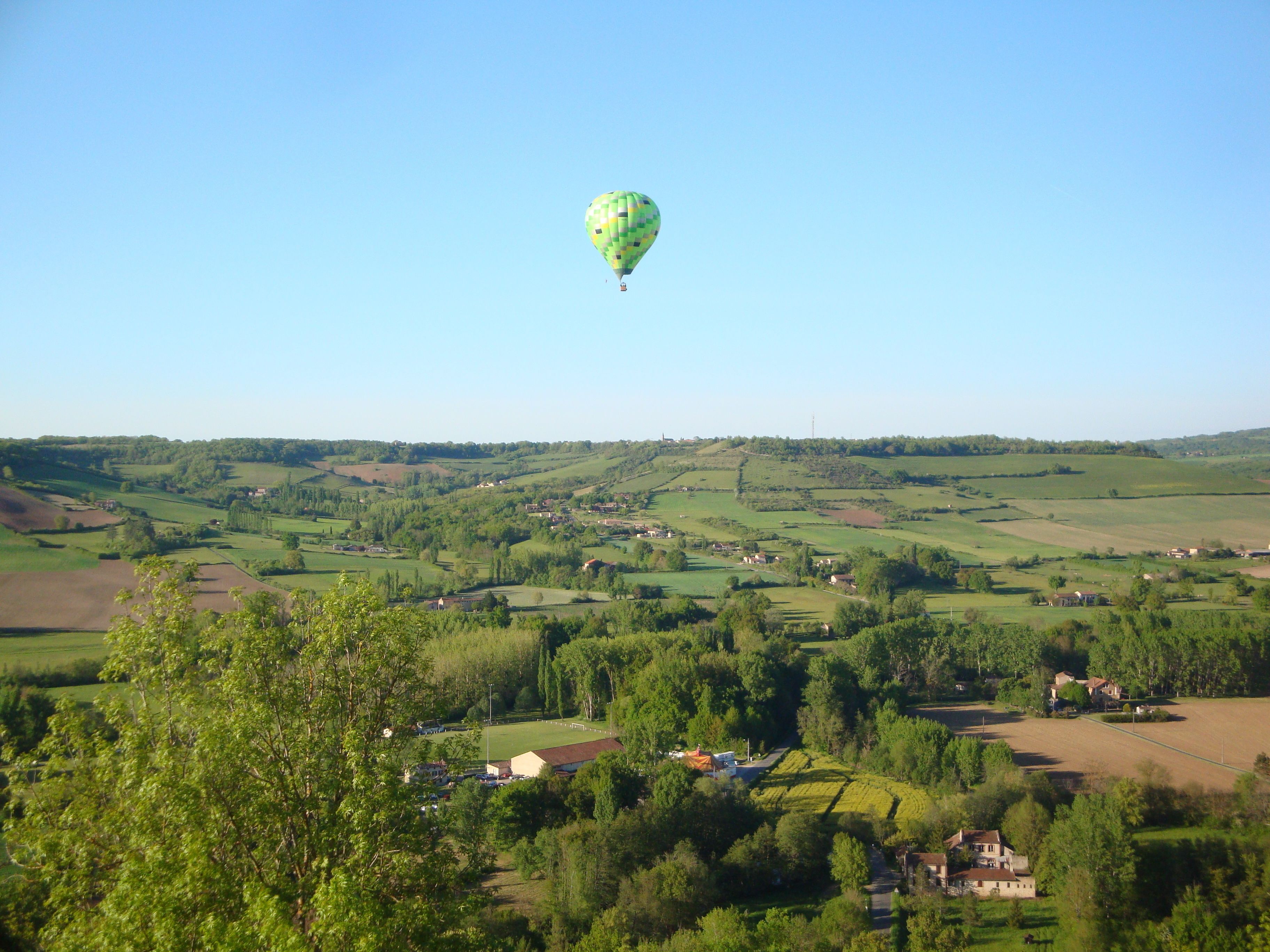 A hot air balloon over a rural landscape with scattered houses and fields.