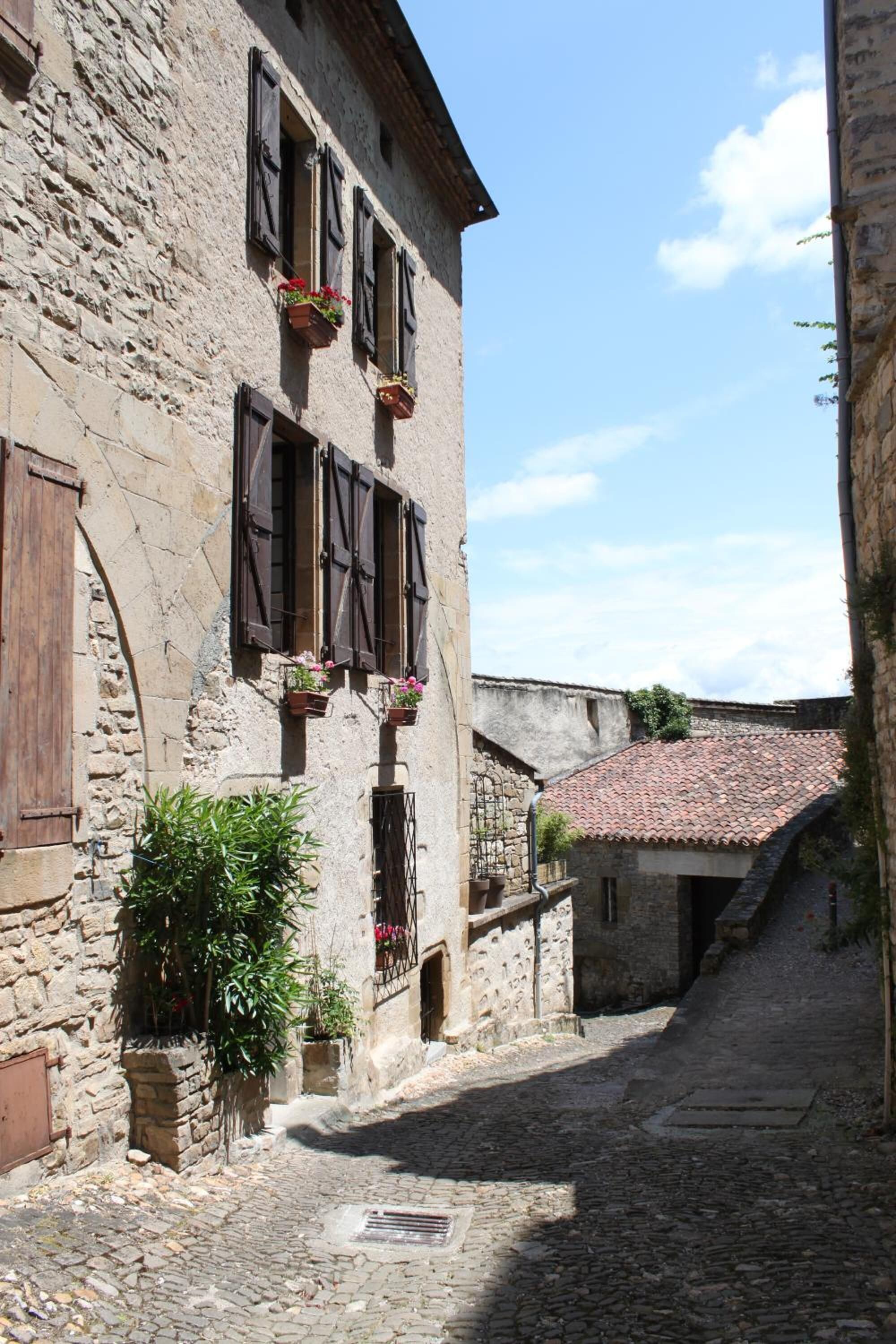 Un carrer empedrat i estret, flanquejat per edificis històrics de pedra amb persianes de fusta i jardineres amb flors.