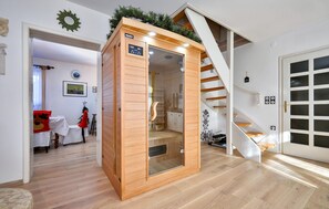 Una sauna de madera con pantalla digital, una escalera y un comedor con un árbol de Navidad.