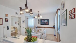 Ein Essbereich mit einem weißen Tisch, gedeckt für zwei Personen, mit einer Ananas und Trauben darauf sowie einem Kronleuchter darüber.
