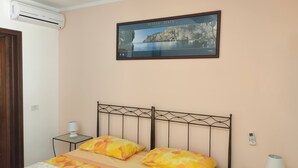A bedroom with a bed, a bedside table with a lamp, a framed picture of a coastal scene, and an air conditioning unit. - B&B Bellavista (Castro)