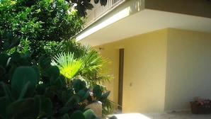 A building with a yellow exterior, a stone-paved entrance, and lush green plants. - B&B Bellavista (Castro)