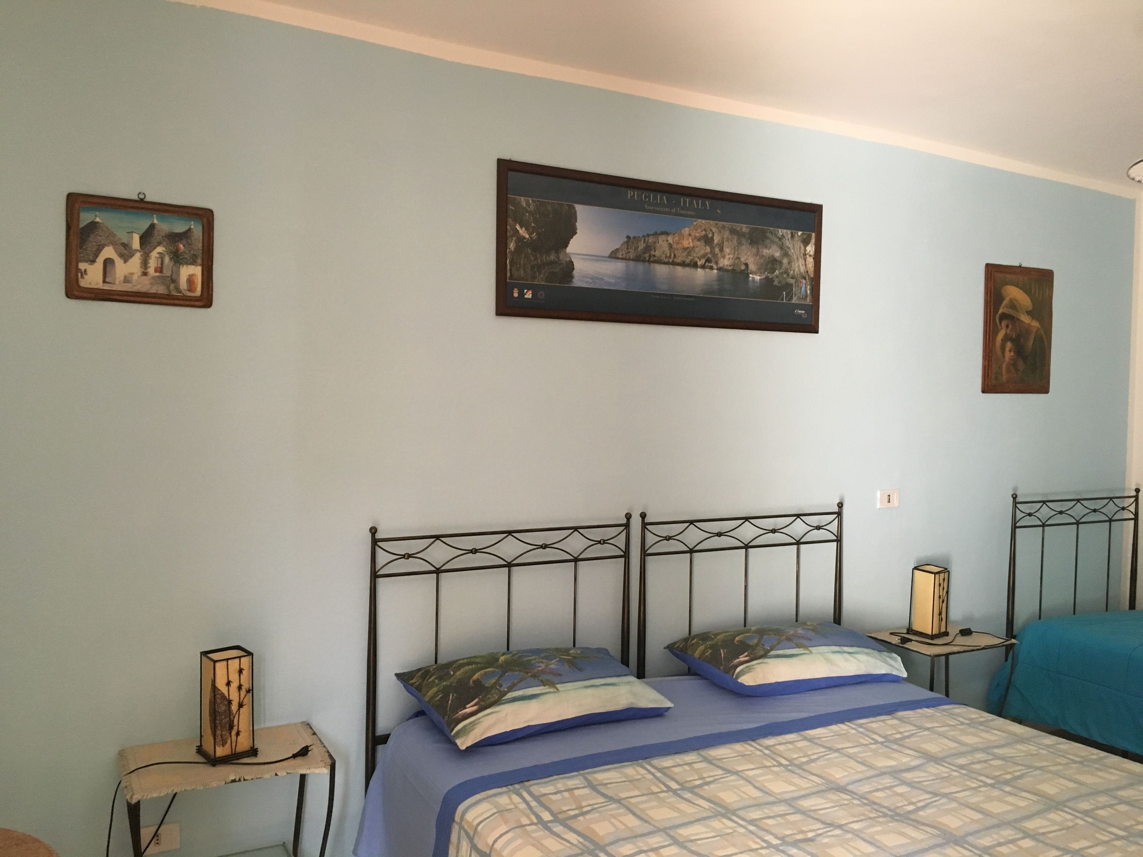 Un dormitorio con cama, dos mesitas de noche, un cuadro en la pared y una fotografía enmarcada sobre la cama.