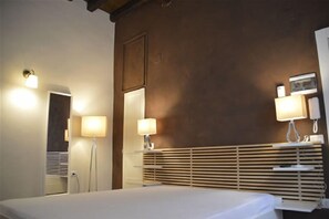 Una habitación de hotel con cama, lámparas de noche, un espejo y cabecera de madera.