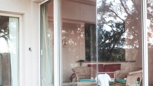 A room with a sliding glass door, wicker furniture, and a view of trees outside. - Andrea Lodges (Riviere des Anguilles)