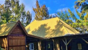 A rustic building with a large wooden barn-like structure on the left, a covered porch with columns, and a gravel driveway leading to the entrance. - Andrea Lodges (Riviere des Anguilles)
