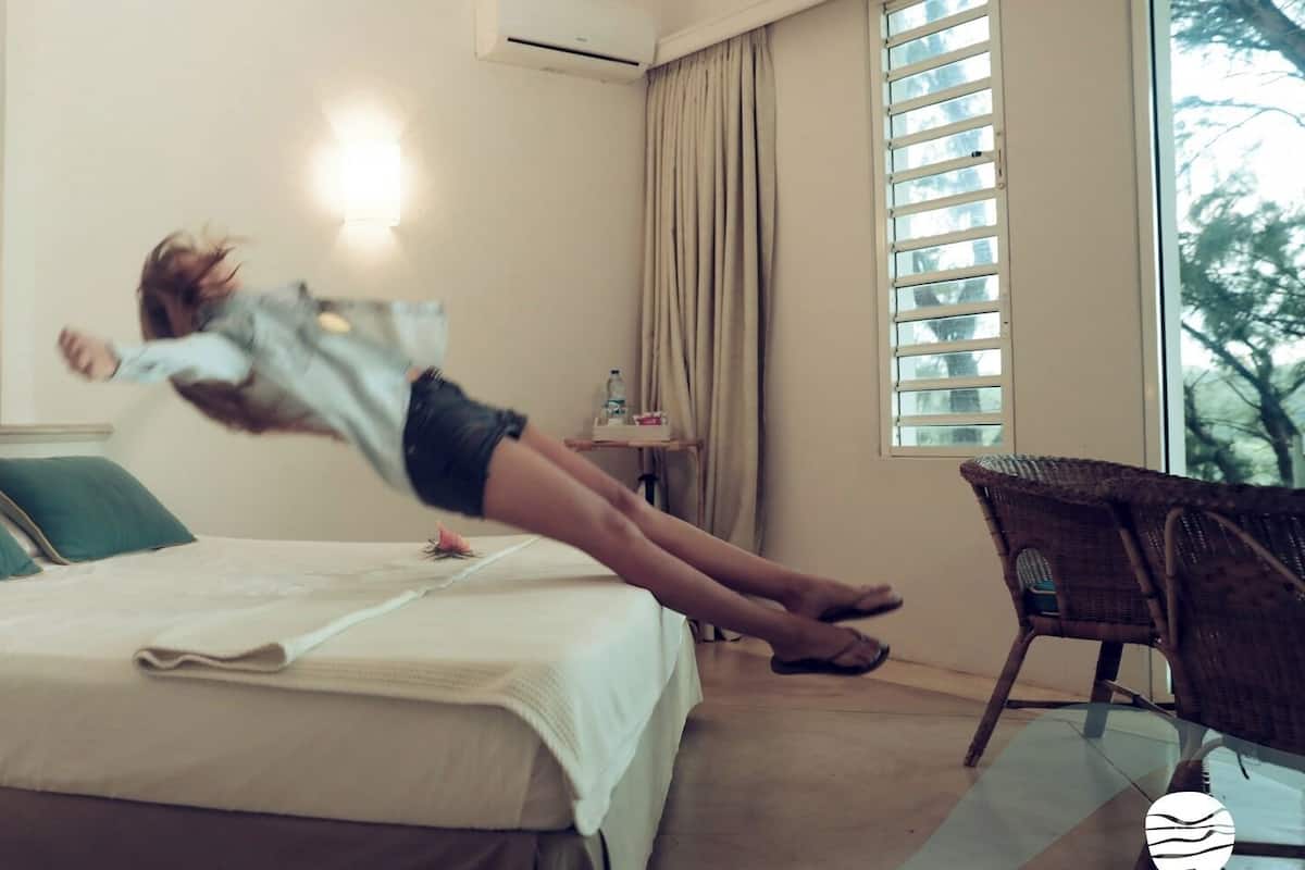 A bedroom with a bed, pillows, a nightstand, a lamp, a window with curtains, and a chair.