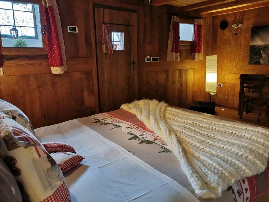 A wooden cabin room with a bed, a blanket, and a window with curtains.