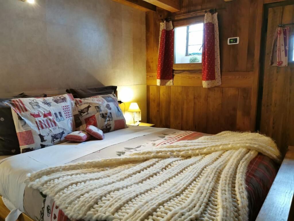 A cozy bedroom with a wooden wall, a bed with patterned bedding, and a window with curtains.