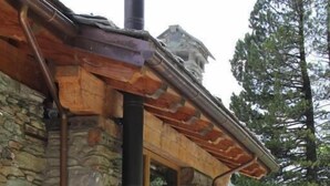 Un edificio de piedra con techo de madera, una chimenea y una hamaca al frente.
