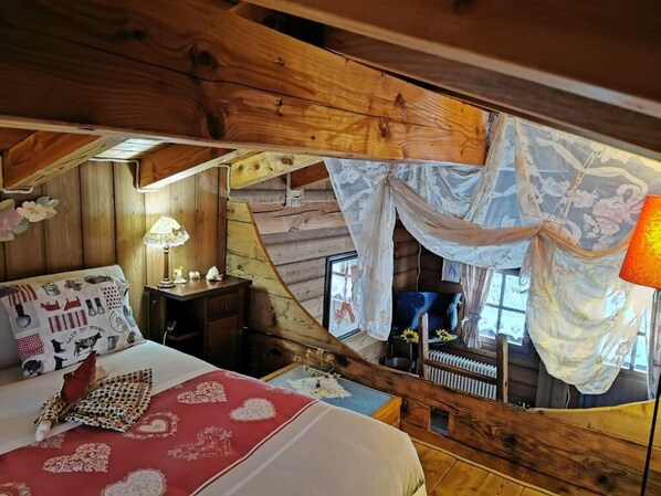 Una habitación acogedora de estilo cabaña con cama, mesita de noche, lámpara y ventana con cortinas translúcidas.