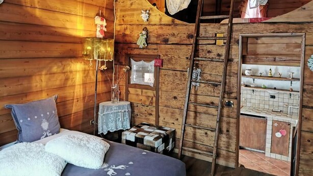 Un dormitorio de cabaña de madera acogedor, con una cama, una escalera, una mesita y una estantería con adornos.