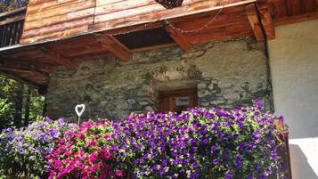 Un edificio de madera con fachada de piedra, un balcón con flores moradas y una decoración con forma de corazón.