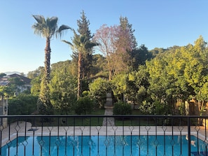 A swimming pool with a metal fence, surrounded by lush greenery and trees. - Kamarca House Hotel (Ortaca)