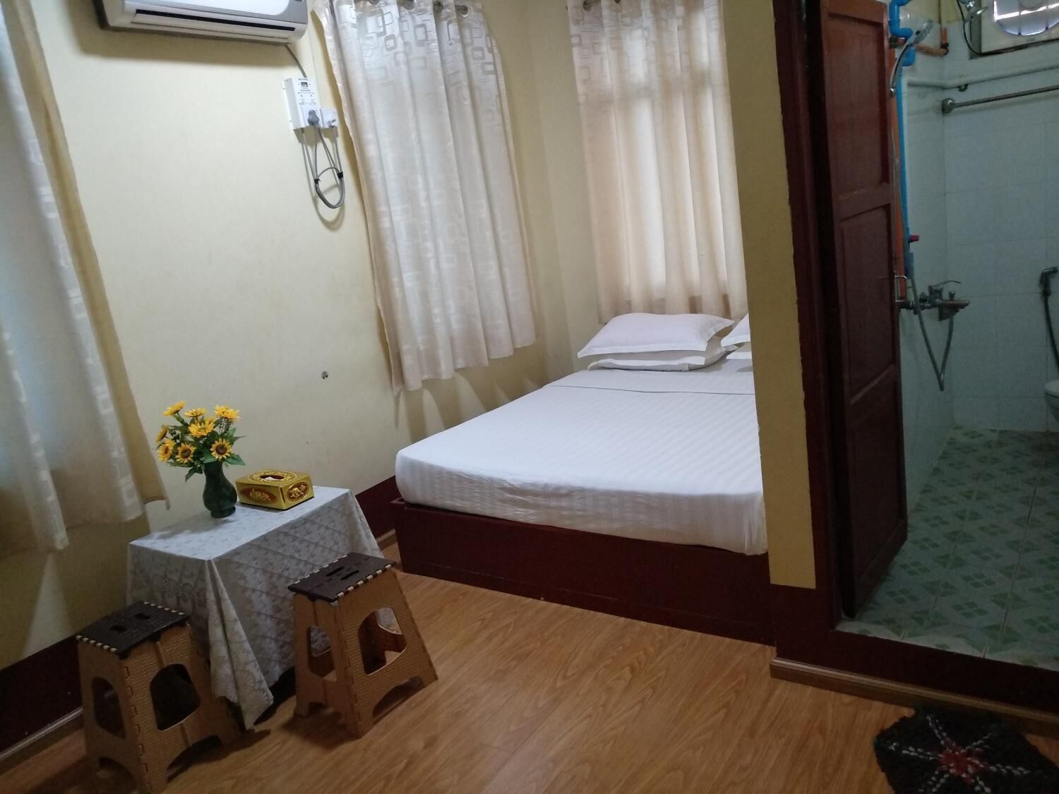 A small room with a bed, a table with a vase of flowers, and a wooden stool.